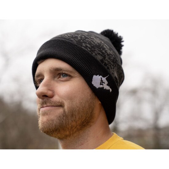 Model wearing the black WVU Nike winter beanie with a pom pom and the state of West Virginia with a Flying WV inside on the front of the cuff